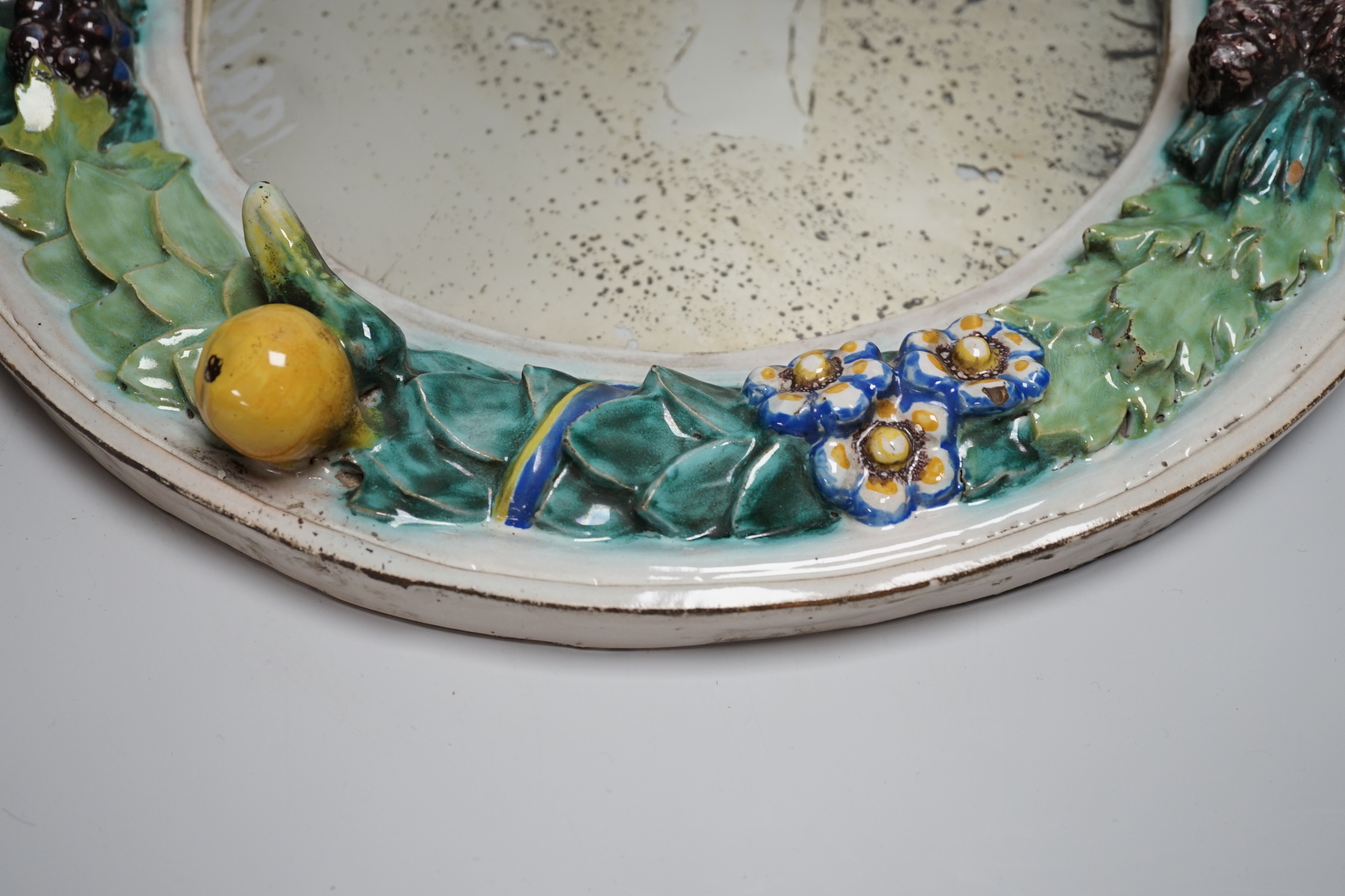 A circular earthenware mirror, possibly by Della Robbia Pottery of Liverpool, decorated with foliage and fruit, 37cm